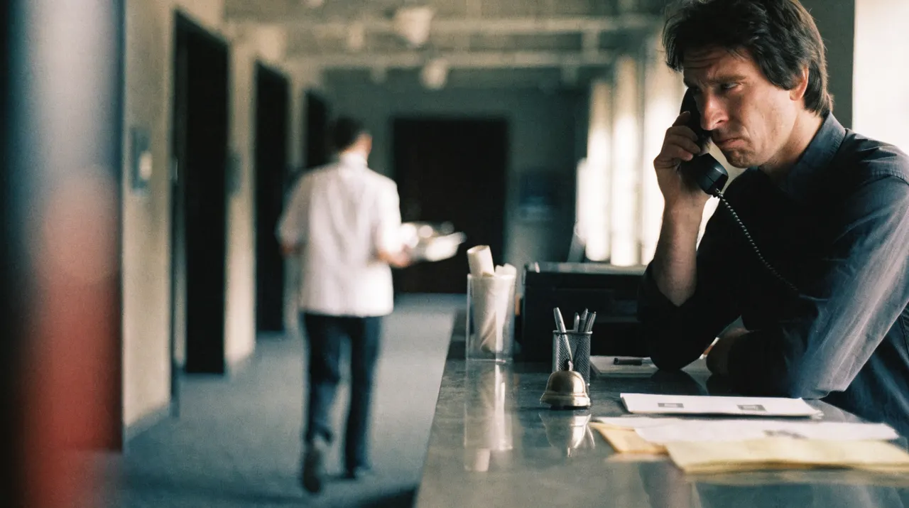 Rezeptionist telefoniert am Empfang, im Hintergrund läuft eine Servicekraft mit Tablett in die falsche Richtung